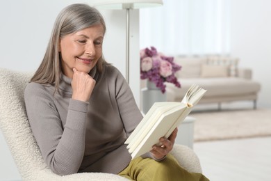 Photo of Beautiful senior woman reading book in armchair at home
