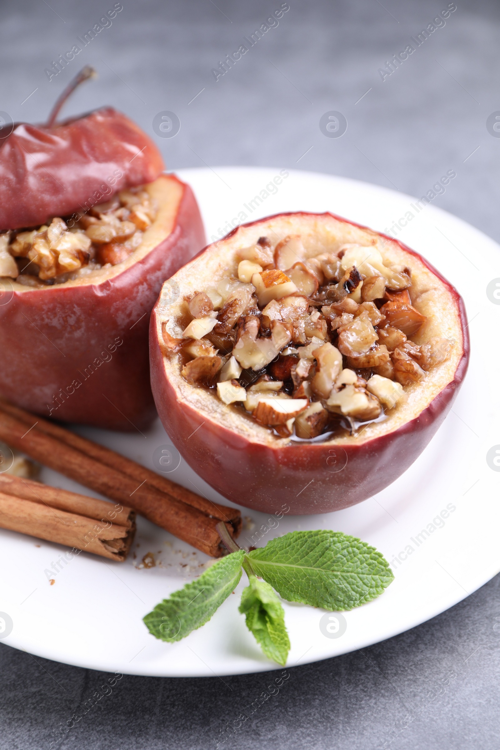 Photo of Tasty baked apples with nuts, honey, cinnamon sticks and mint on gray table, closeup