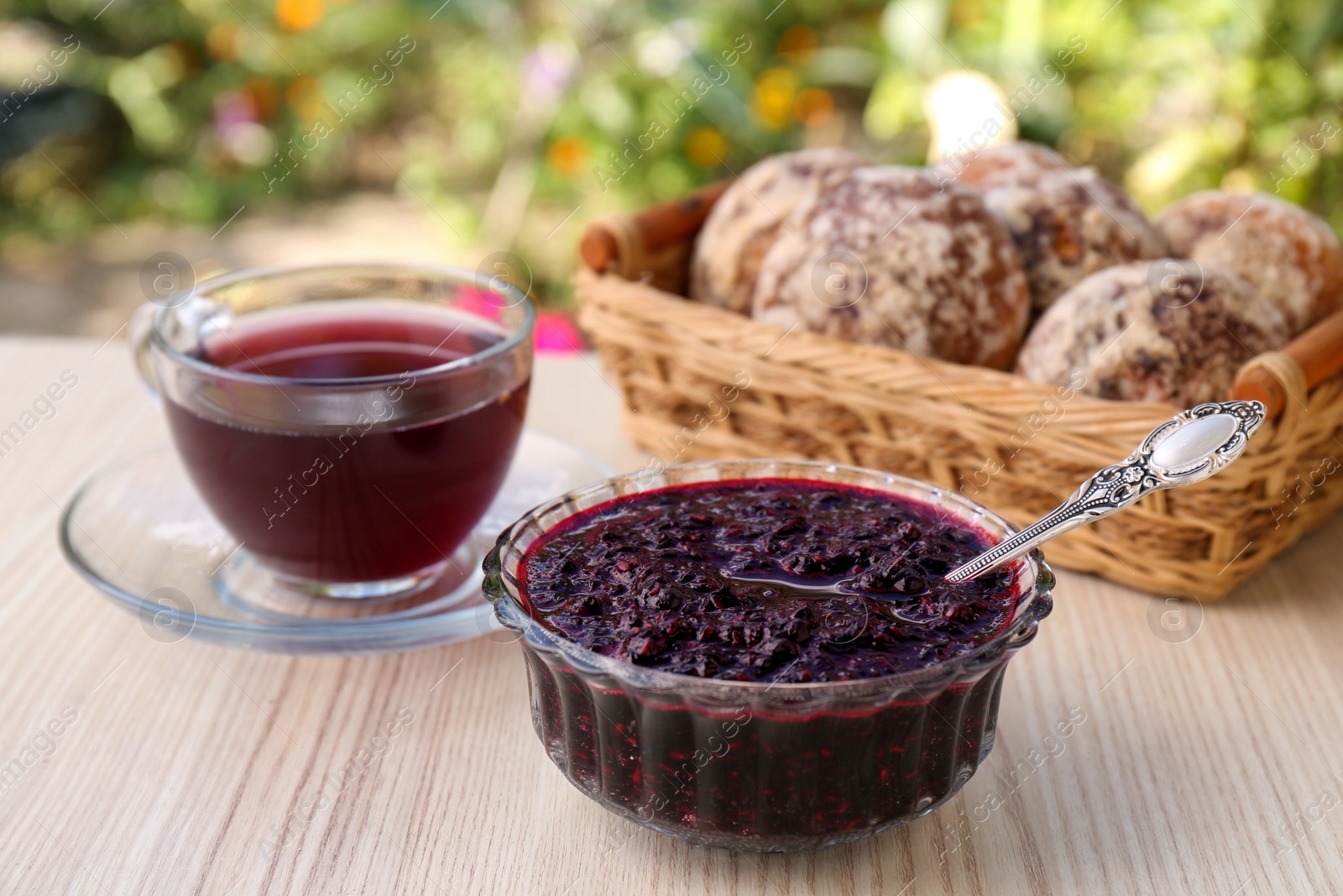 Photo of Elderberry (Sambucus) jam, glass cup of tea and tasty cookies on wooden table outdoors