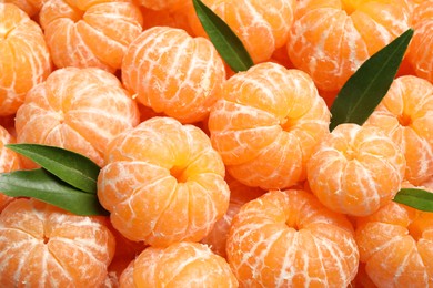 Photo of Peeled fresh ripe tangerines with green leaves as background, closeup