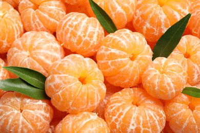 Peeled fresh ripe tangerines with green leaves as background, closeup