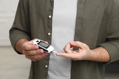 Photo of Diabetes test. Man checking blood sugar level with glucometer at home, closeup