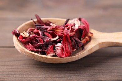 Photo of Spoon of dry hibiscus tea on wooden table, closeup