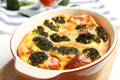 Photo of Tasty broccoli casserole in baking dish on wooden board, closeup