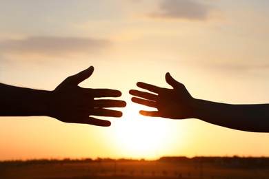 Photo of Man and woman reaching out at sunset. Help and support concept