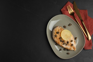 Photo of Delicious chicken fillet with capers and lemon served on black table, flat lay. Space for text