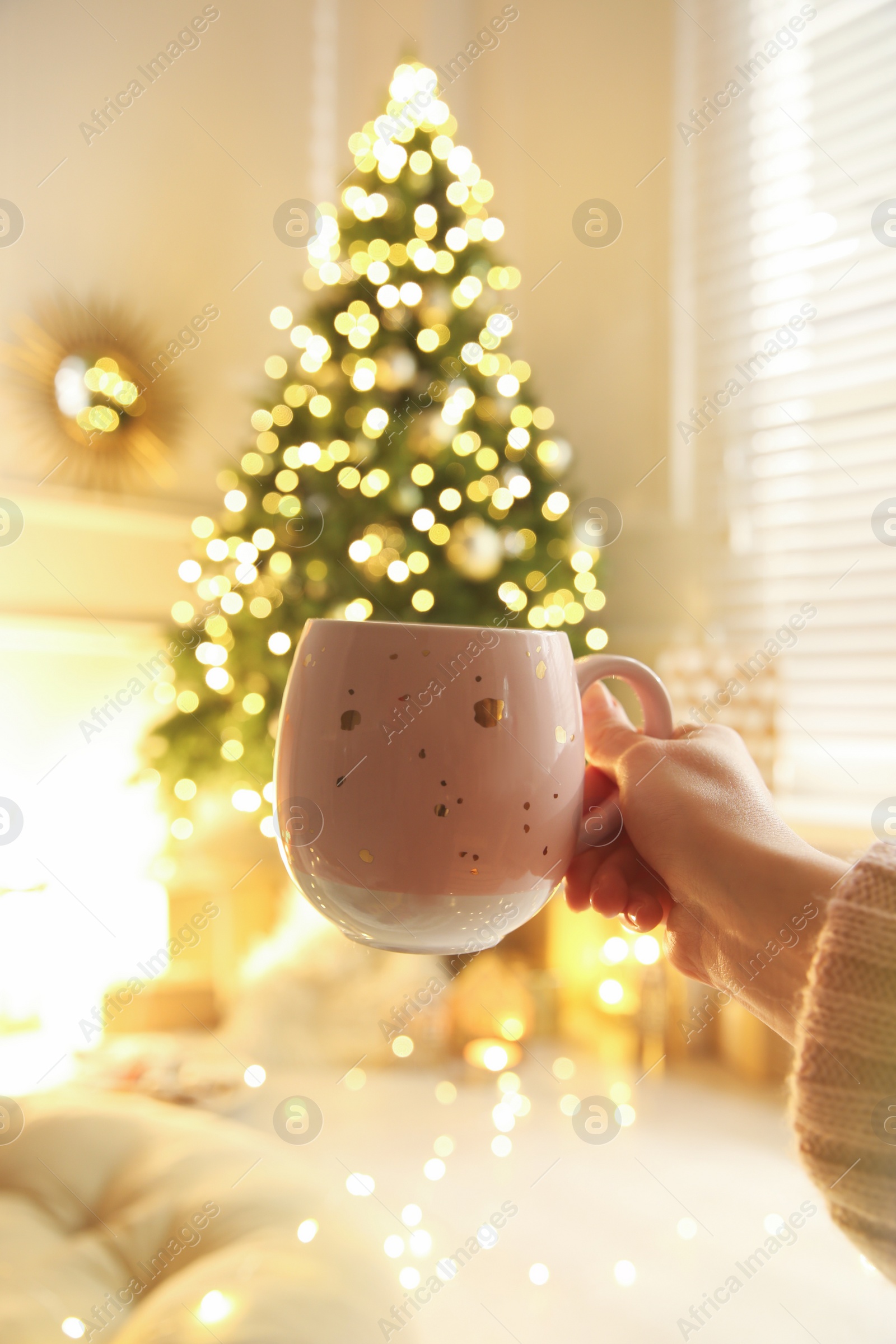 Photo of Woman with cup of drink and blurred Christmas tree on background, closeup