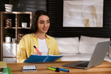 Photo of Young woman watching webinar at table in room