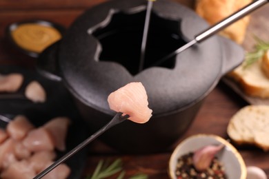 Fork with piece of raw meat over fondue pot, closeup
