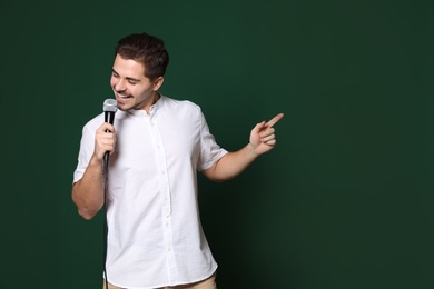 Photo of Young handsome man in casual clothes singing with microphone on color background. Space for text