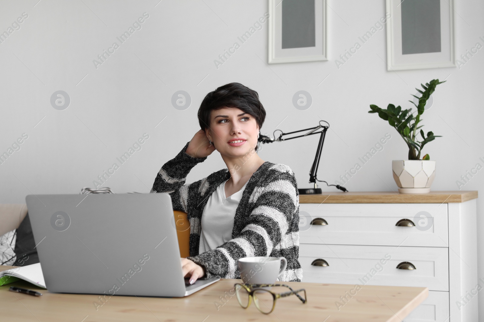 Photo of Young woman working with laptop at desk. Home office