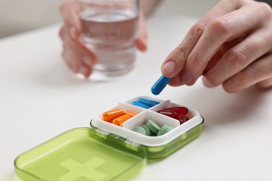 Woman with pills, organizer and glass of water at white table, closeup