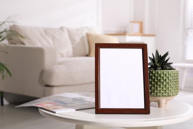 Photo of Empty photo frame, magazine and succulent on white table in living room, space for text