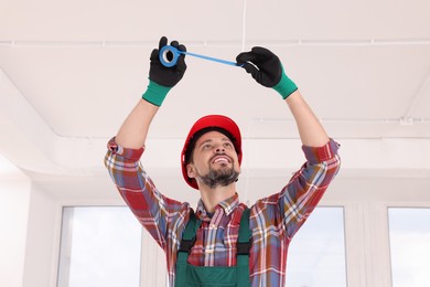 Electrician in uniform with insulating tape repairing ceiling wiring indoors
