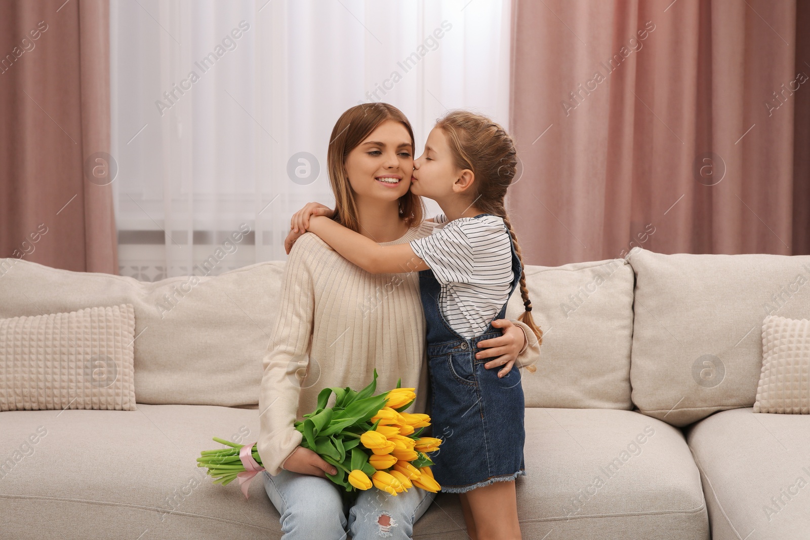 Photo of Little daughter congratulating mom with bouquet of yellow tulips at home. Happy Mother's Day