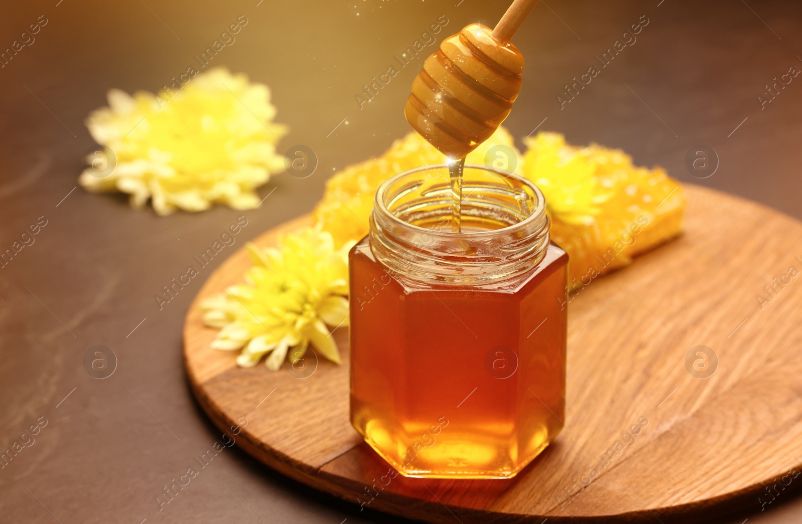 Image of Natural honey dripping from dipper into glass jar on table under sunlight