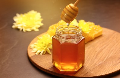 Natural honey dripping from dipper into glass jar on table under sunlight