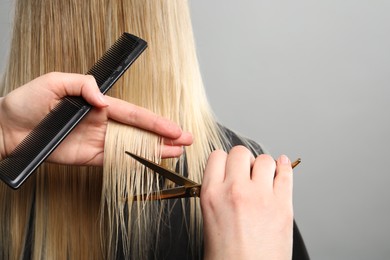 Photo of Hairdresser cutting client's hair with scissors on light grey background, closeup. Space for text