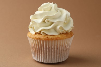 Photo of Tasty vanilla cupcake with cream on dark beige background, closeup