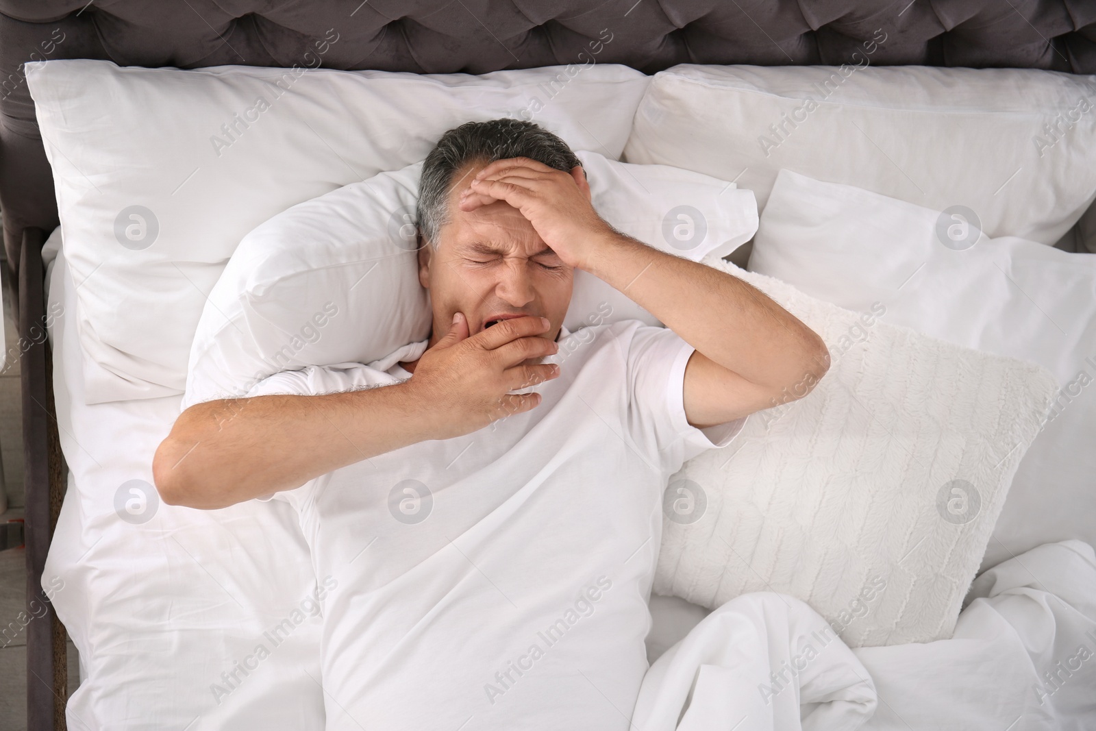 Photo of Man yawning after sleeping on comfortable pillow in bed at home