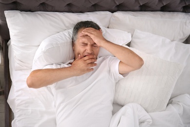 Man yawning after sleeping on comfortable pillow in bed at home