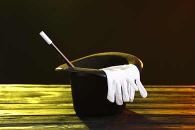 Photo of Magician's hat, wand and gloves on wooden table against black background