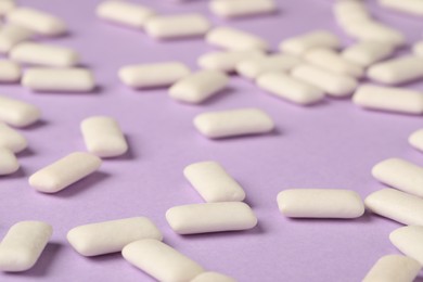 Photo of Many chewing gum pieces on violet background, closeup