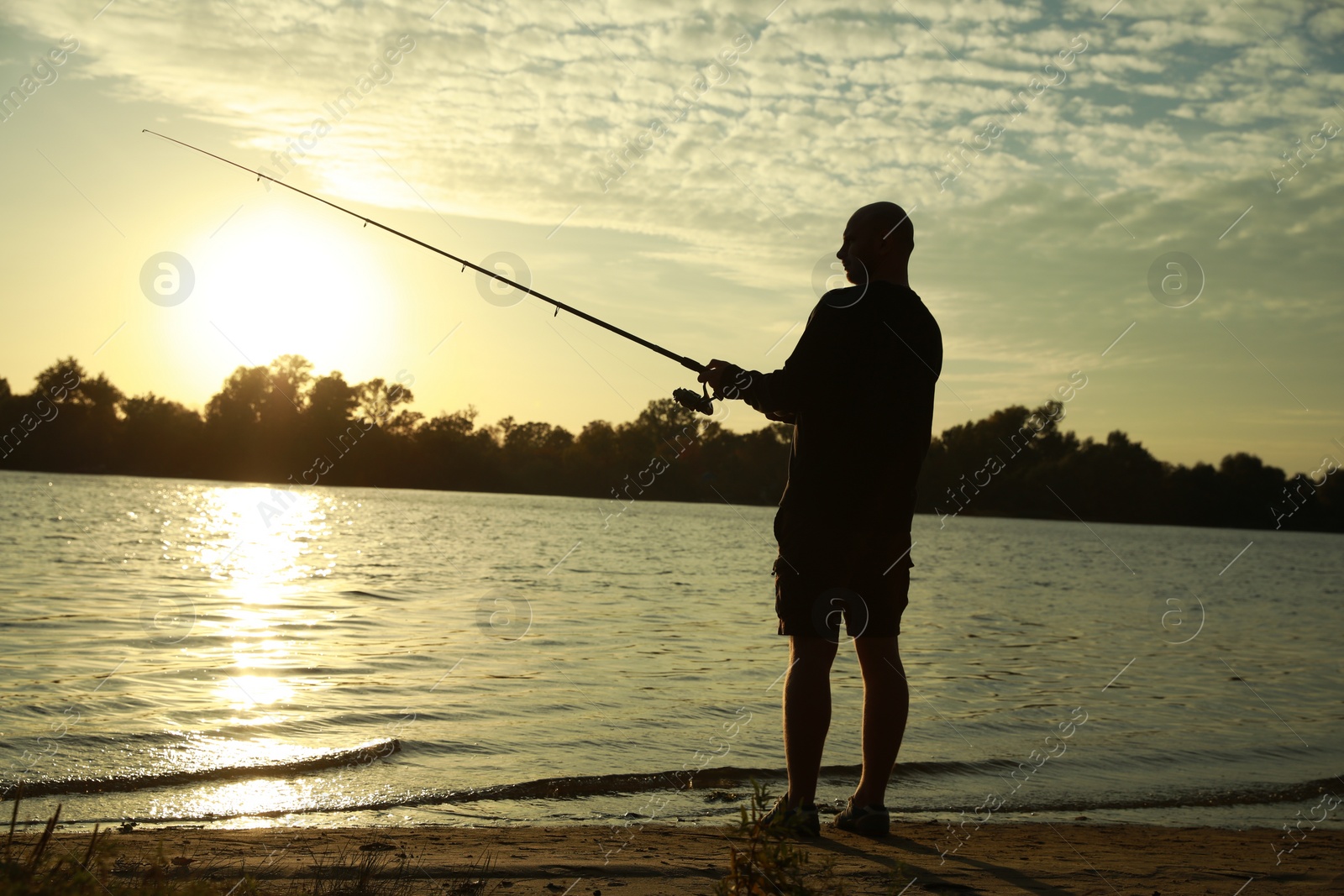 Photo of Fisherman with rod fishing at riverside at sunset