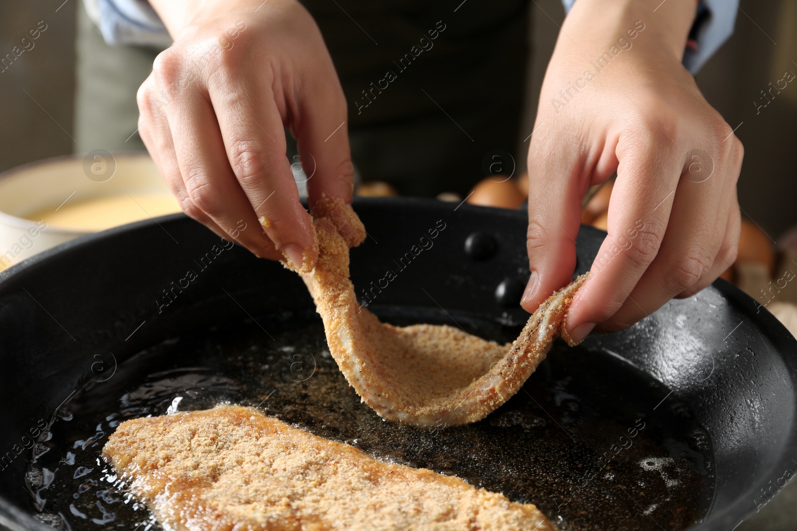 Photo of Cooking schnitzel. Woman putting raw pork chop in bread crumbs into frying pan, closeup