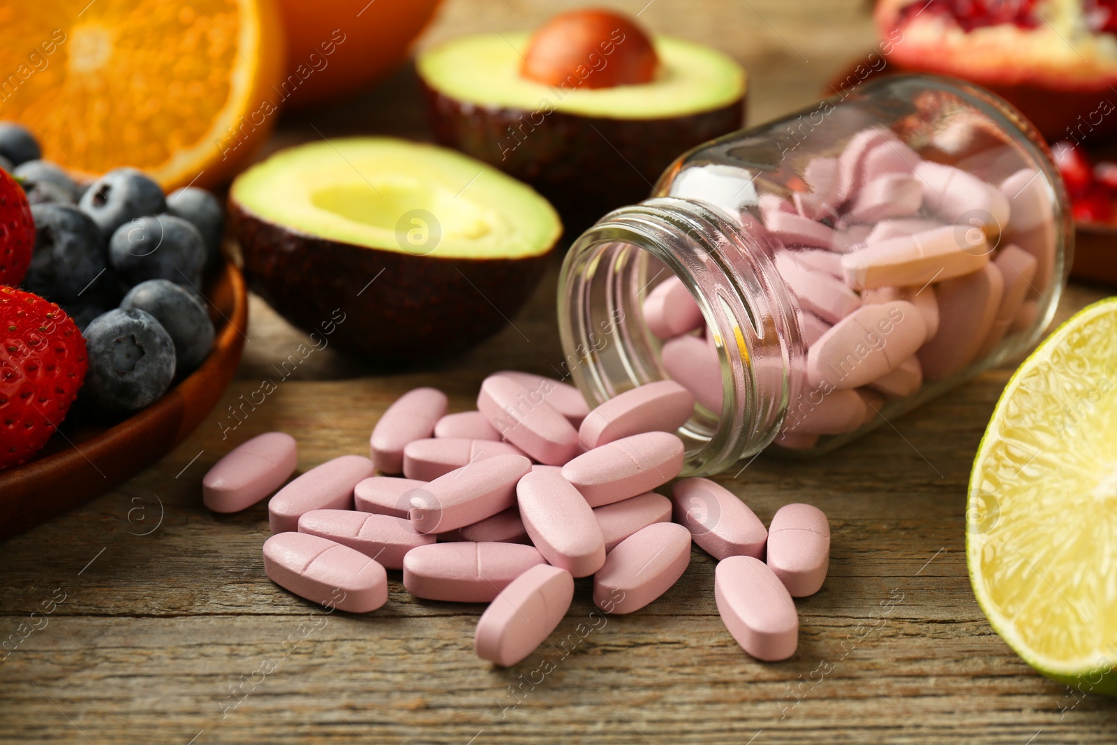 Photo of Vitamin pills in bottle and fresh fruits on wooden table, closeup