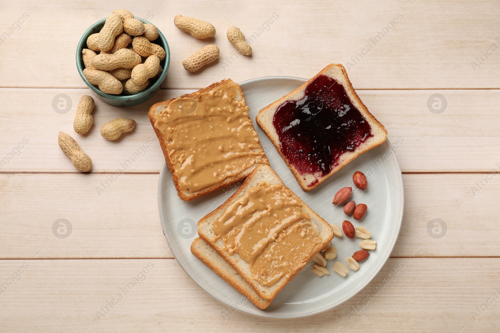 Photo of Delicious toasts with peanut butter, jam and nuts on light wooden table, flat lay