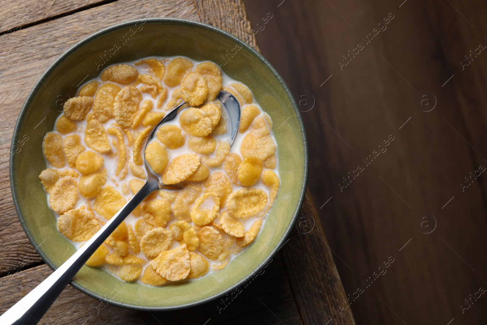 Photo of Tasty cornflakes with milk in bowl on wooden table, top view. Space for text