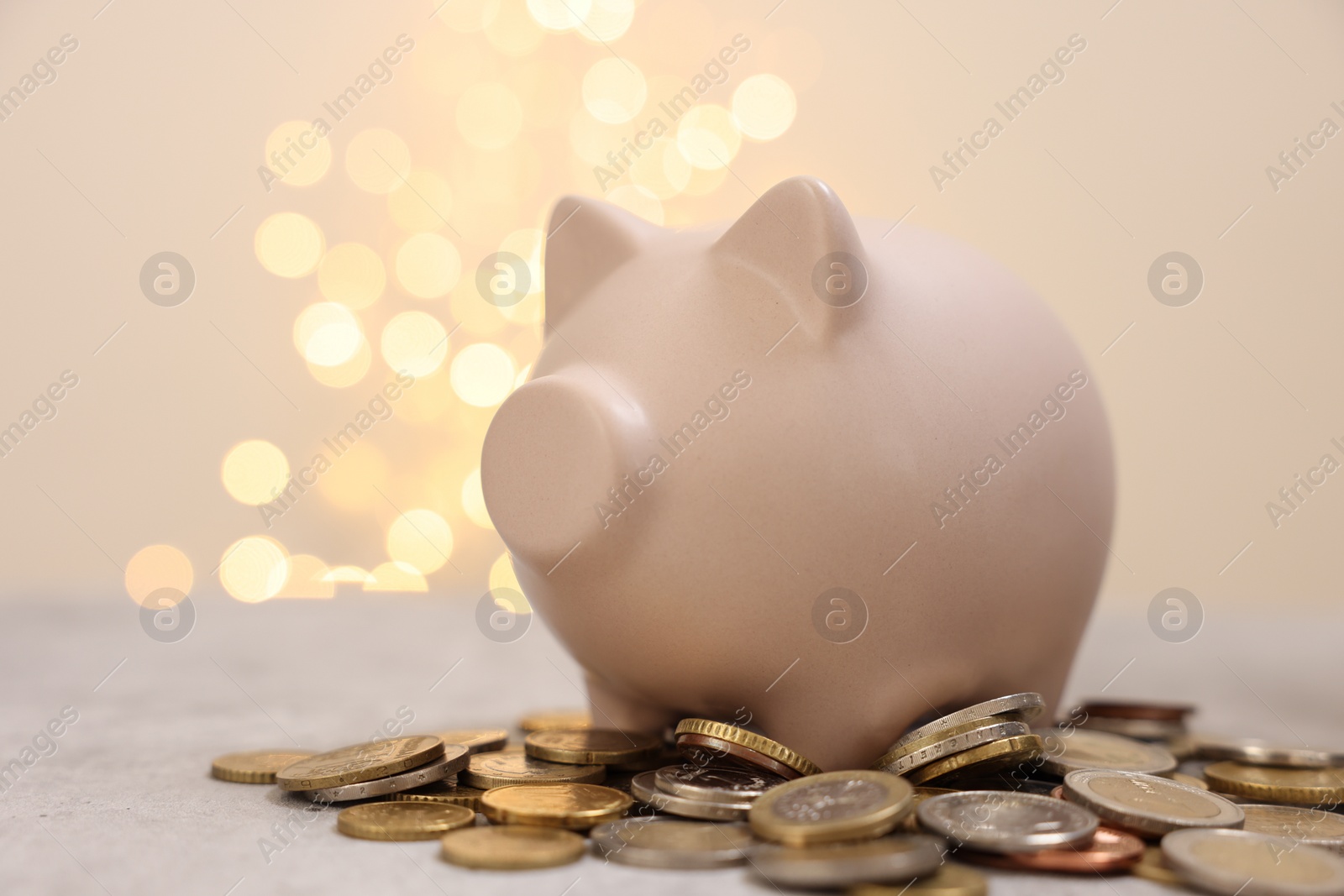 Photo of Piggy bank and coins on grey table against blurred lights