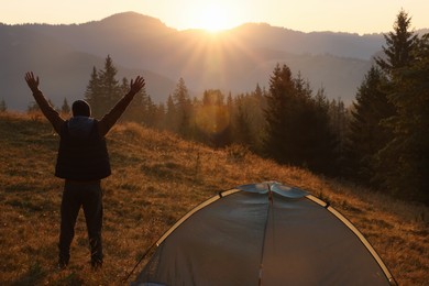 Photo of Tourist enjoying sunrise near camping tent in mountains, back view