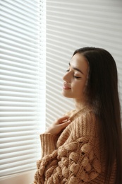Photo of Young woman near window with Venetian blinds