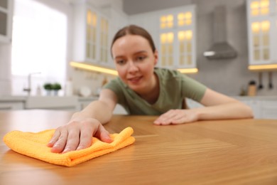 Photo of Woman with microfiber cloth cleaning wooden table in kitchen, selective focus