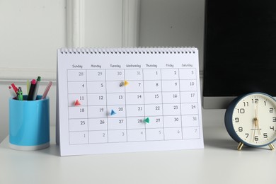 Photo of Timetable. Calendar with marked dates, alarm clock and stationery on white table indoors