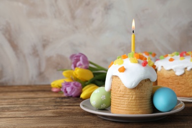 Photo of Easter cakes, colorful eggs and tulips on wooden table, space for text