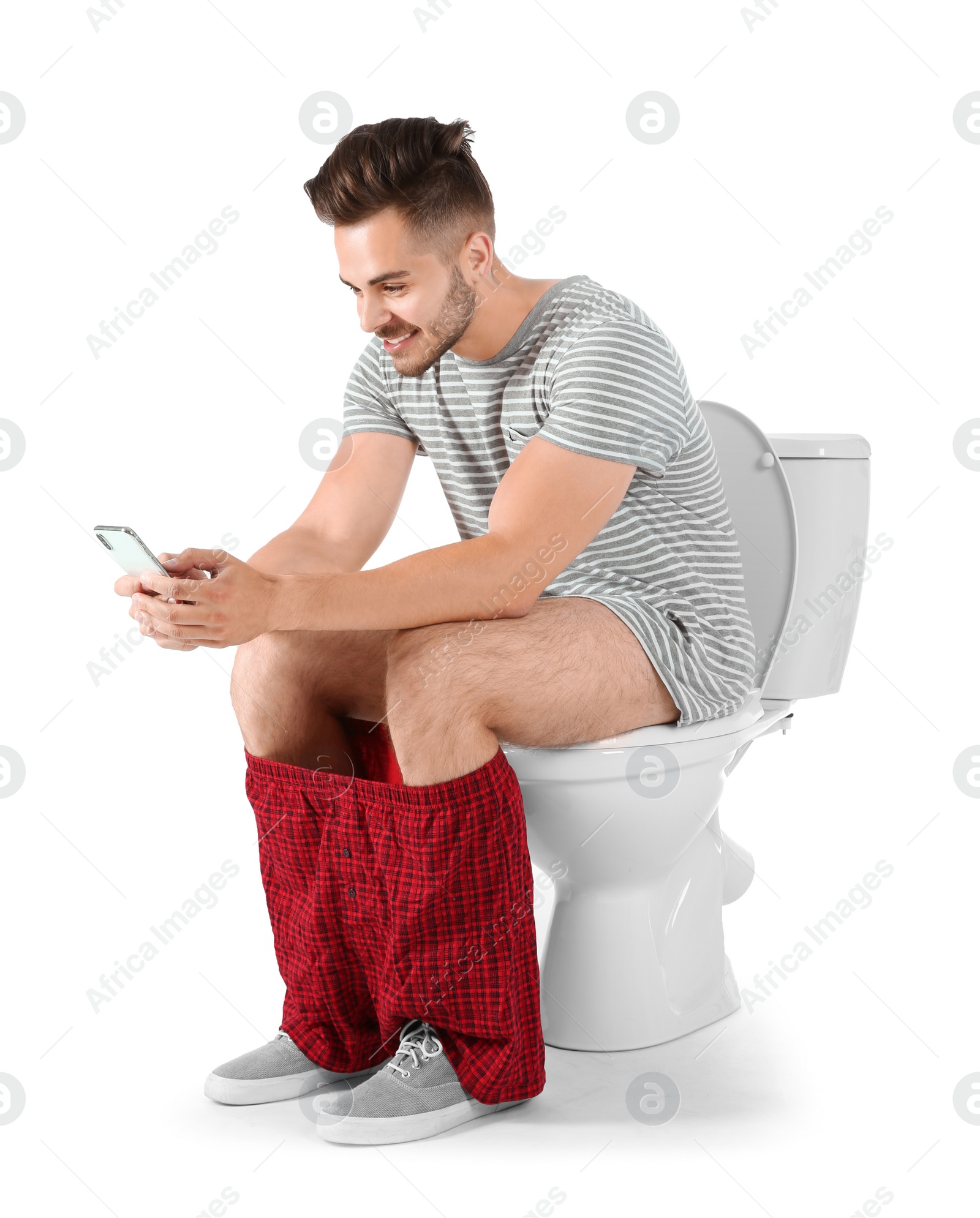 Photo of Young man using mobile phone while sitting on toilet bowl. Isolated on white