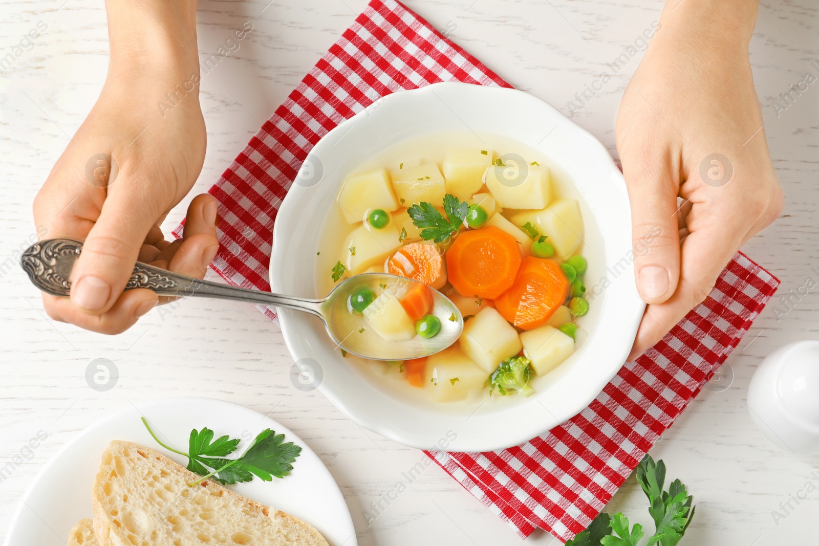 Photo of Woman eating fresh homemade vegetable soup at white wooden table, top view