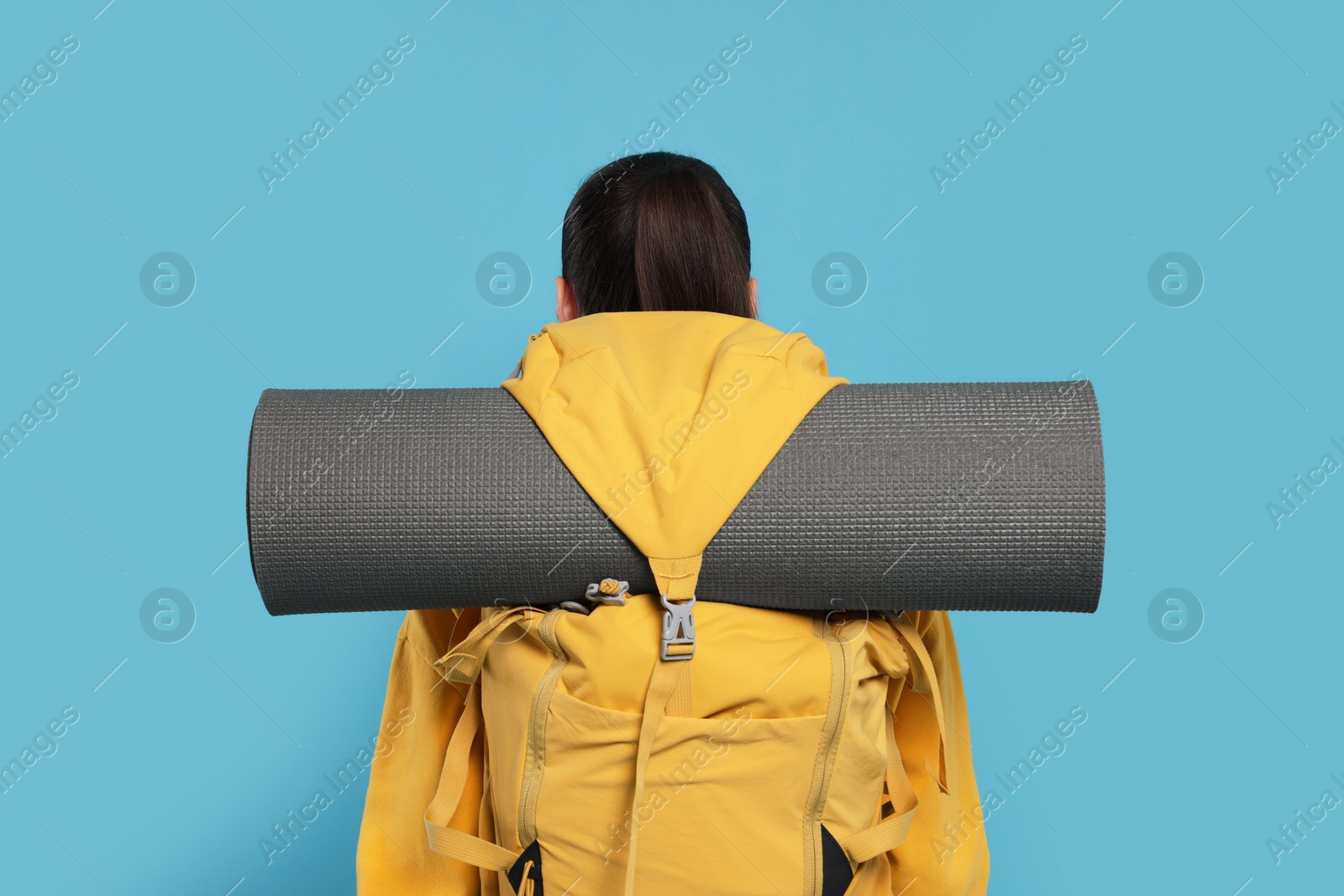 Photo of Woman with backpack and mat on light blue background, back view. Active tourism