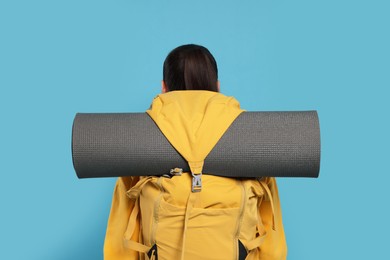 Photo of Woman with backpack and mat on light blue background, back view. Active tourism