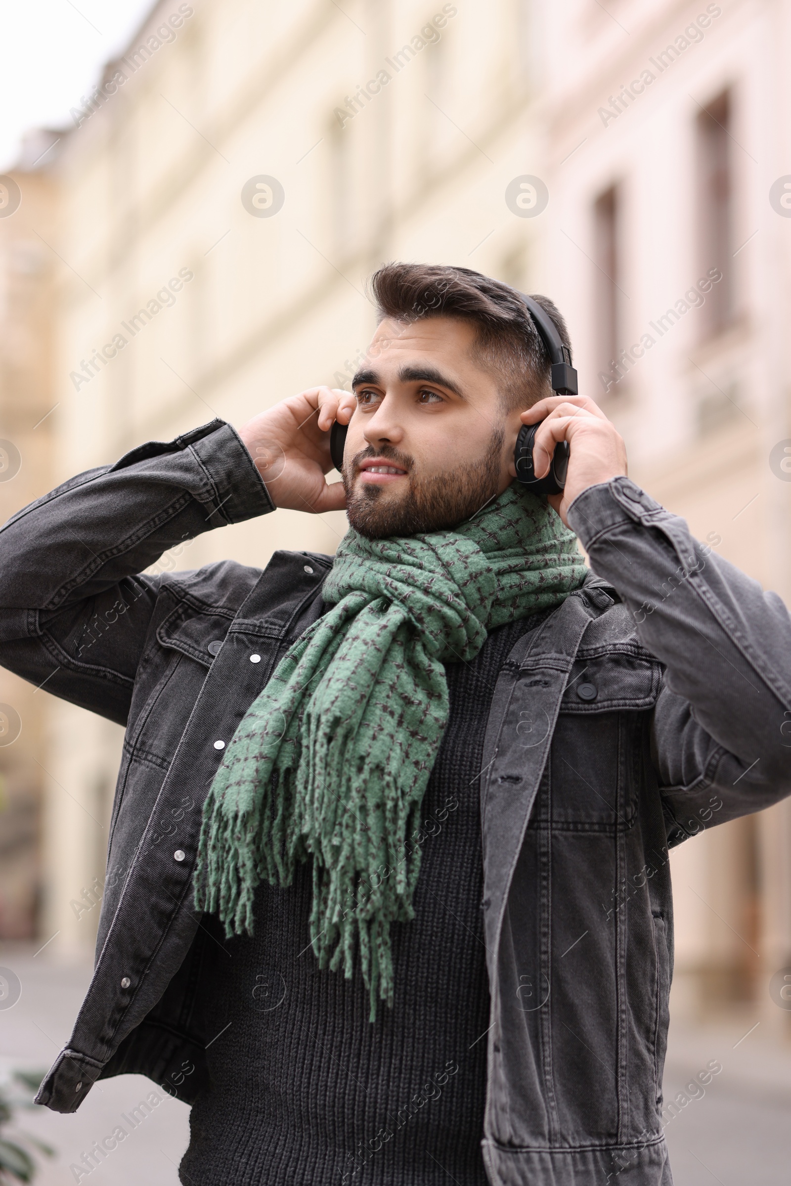 Photo of Smiling man in warm scarf listening to music outdoors