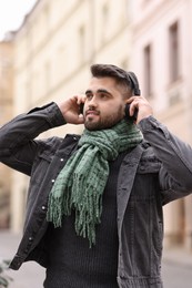 Photo of Smiling man in warm scarf listening to music outdoors