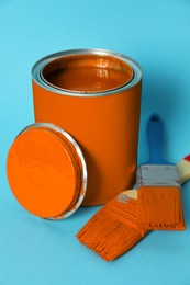 Photo of Can of orange paint and brushes on turquoise background