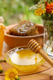 Photo of Delicious honey flowing down from dipper into bowl on wooden board in garden