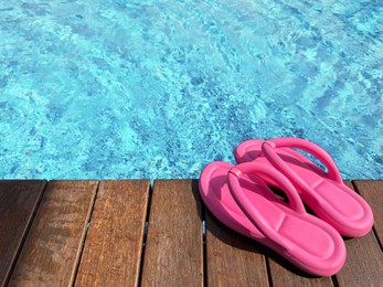 Photo of Clear rippled water in swimming pool and pink flip-flops on wooden deck outdoors. Space for text