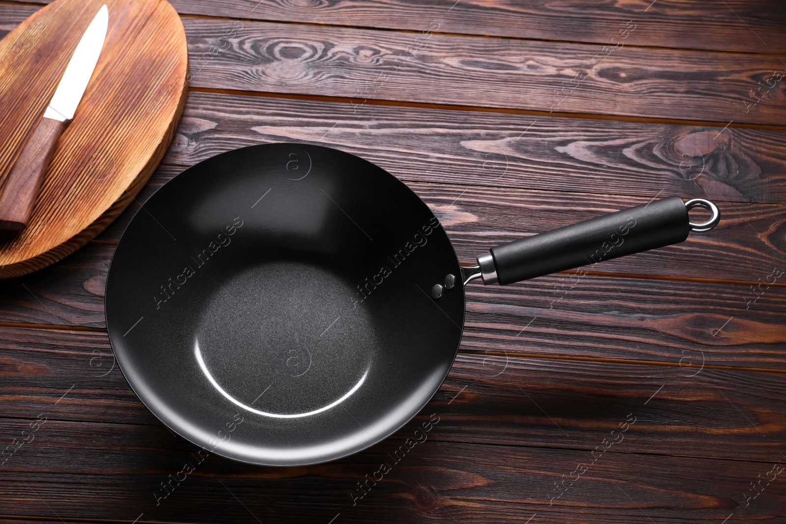 Photo of Empty iron wok, knife and cutting board on wooden table