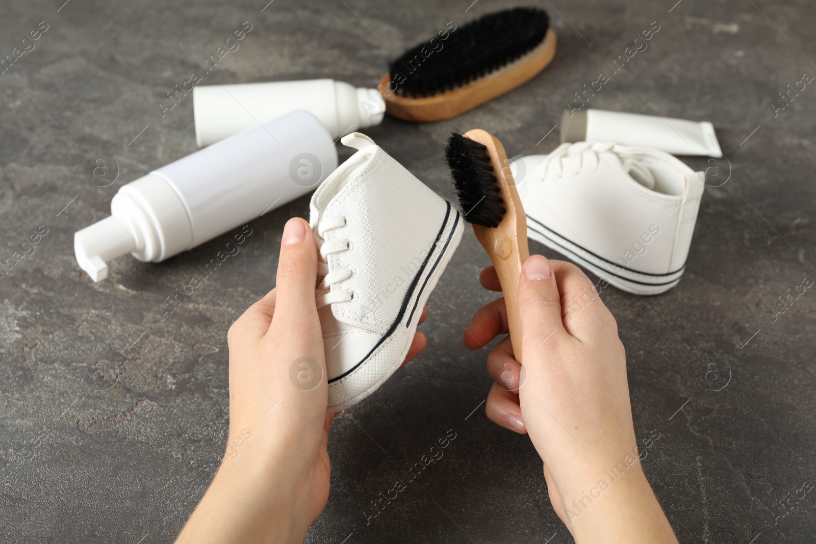 Photo of Woman cleaning stylish footwear on grey stone background, closeup. Shoe care accessories