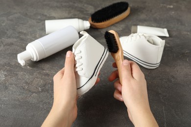 Woman cleaning stylish footwear on grey stone background, closeup. Shoe care accessories